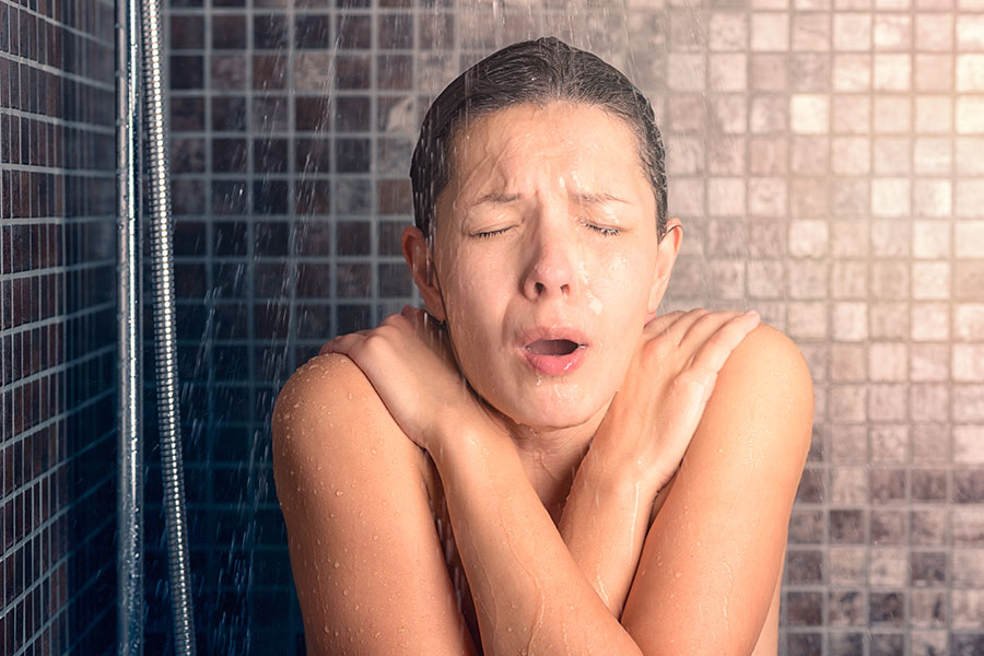 Woman taking a cold shower because her water heater is experiencing problems. She requires professional water repair services in Collinsville, IL.