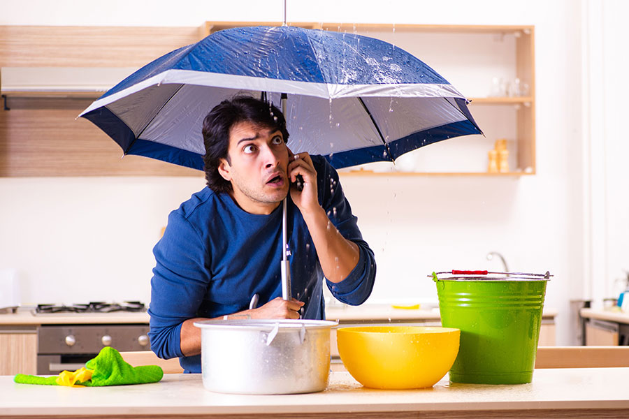 Man on the phone under an umbrella in the kitchen with a plumber in the Metro East, IL area requesting emergency plumbing services for a leak.